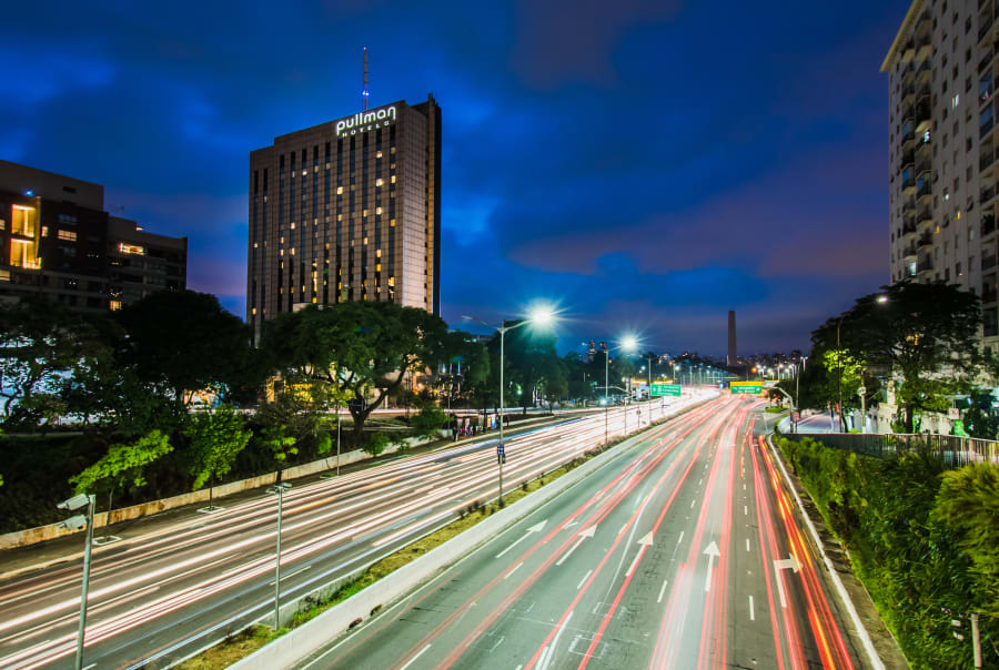 Pullman Ibirapuera tower at blue hour above an avenue streaked with car light trails
