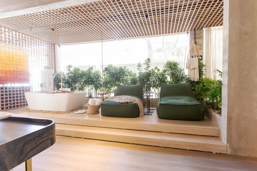 Freestanding tub and green lounge cushions on a raised planted deck under a timber grid ceiling