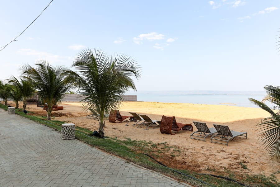 Coconut palms and sun loungers on a sandy river beach beside a paved promenade