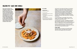 Teller mit cremigen Rigatoni, darüber frischer Parmesan, eine Hand streut Käse auf die orangefarbene Pasta.