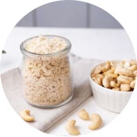 Veganer Cashewparmesan in einem Glas, daneben Cashewnüsse