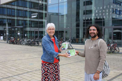 Die Klimadezernentin Gerda Weigel-Greilich drückt einem Gießener ein Klimasparbuch in die Hand. Beide lächeln in die Kamera.