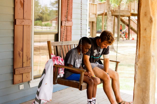 A camper and counselor pray together on a cabin swing