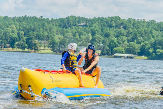 Camper at Pine Cove Shores, a high school Christian summer camp in Tyler, TX, has fun while safely riding the banana boat with his counselor