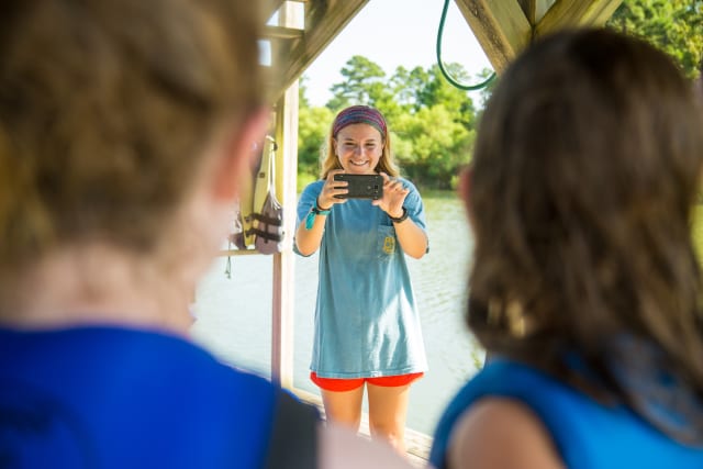 Girl takes a photo with a phone of campers on a dock