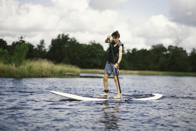Camper rides a stand up paddleboard across the lake at the Ridge camp