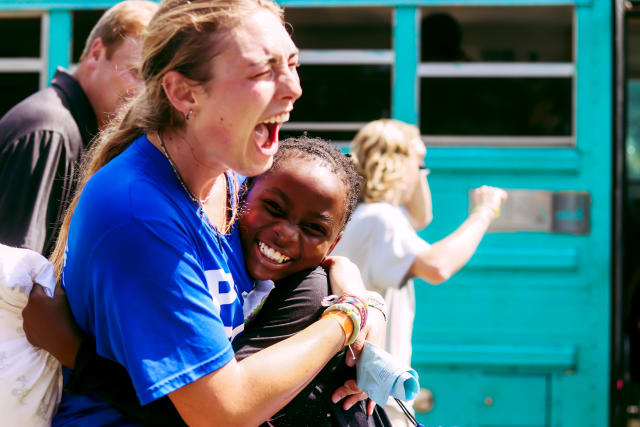 A girl gives a summer staffer a hug after exiting the bus