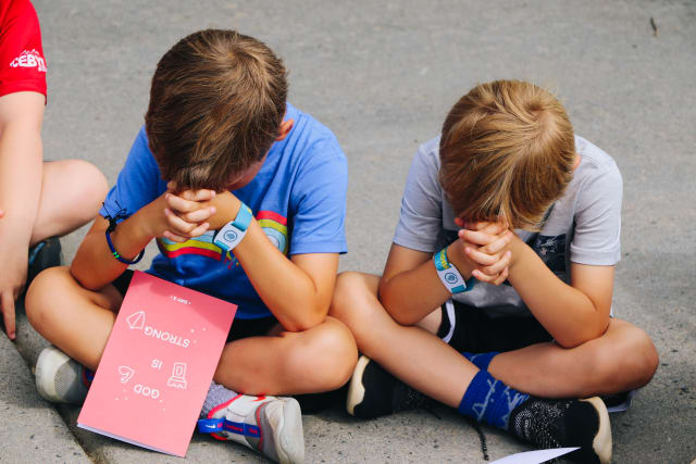 Two boys pray together with their heads bowed and hands folded