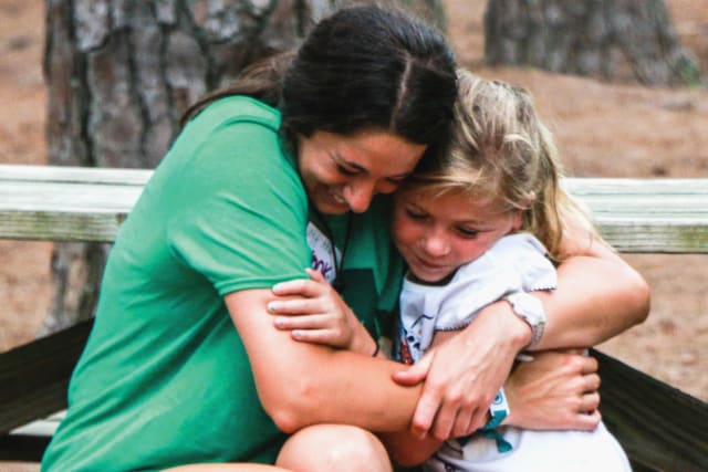 Girl counselor and camper hug on a picnic table.