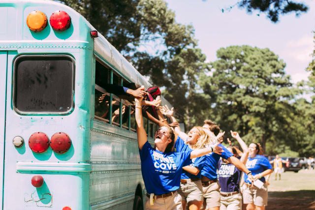 Summer staff give high fives to kids arriving on a bus