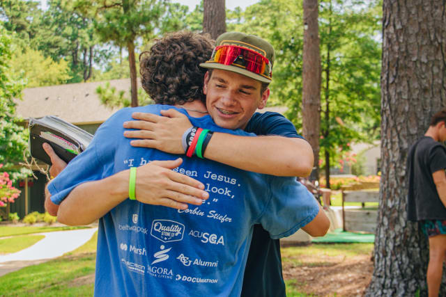 Girl counselor and camper hug on a picnic table.