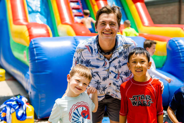 Two City campers smile with their counselor in front of a giant inflatable water slide