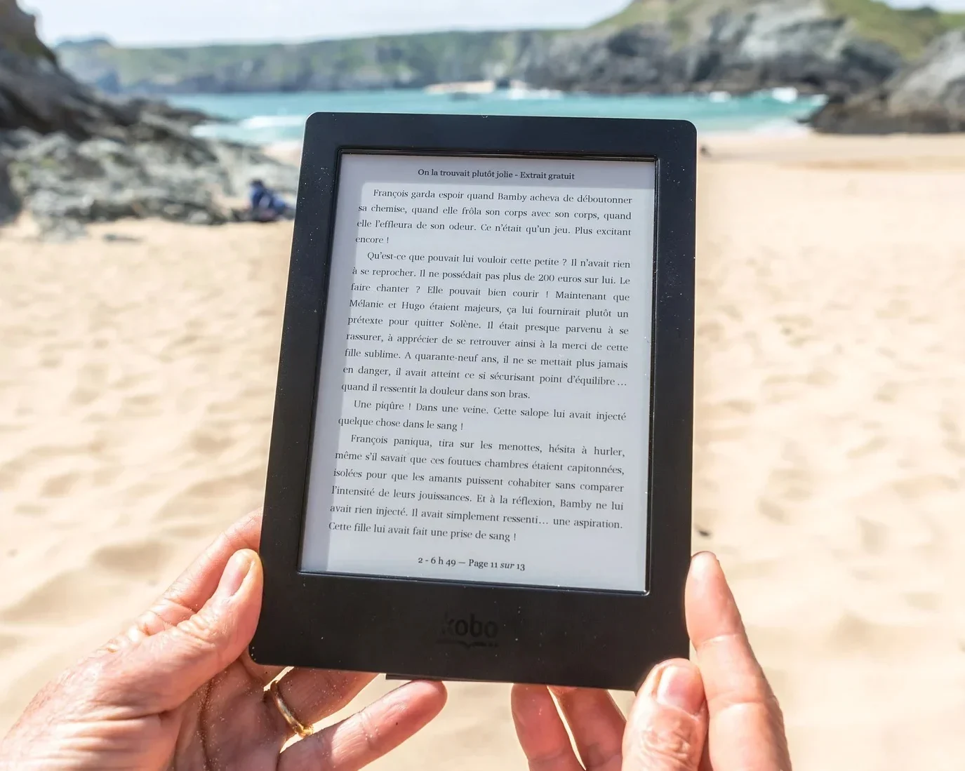 Foto de duas mãos segurando um kindle e uma paisagem de praia ao fundo. Podia ser eu, mas o Brasil não colabora.<br>