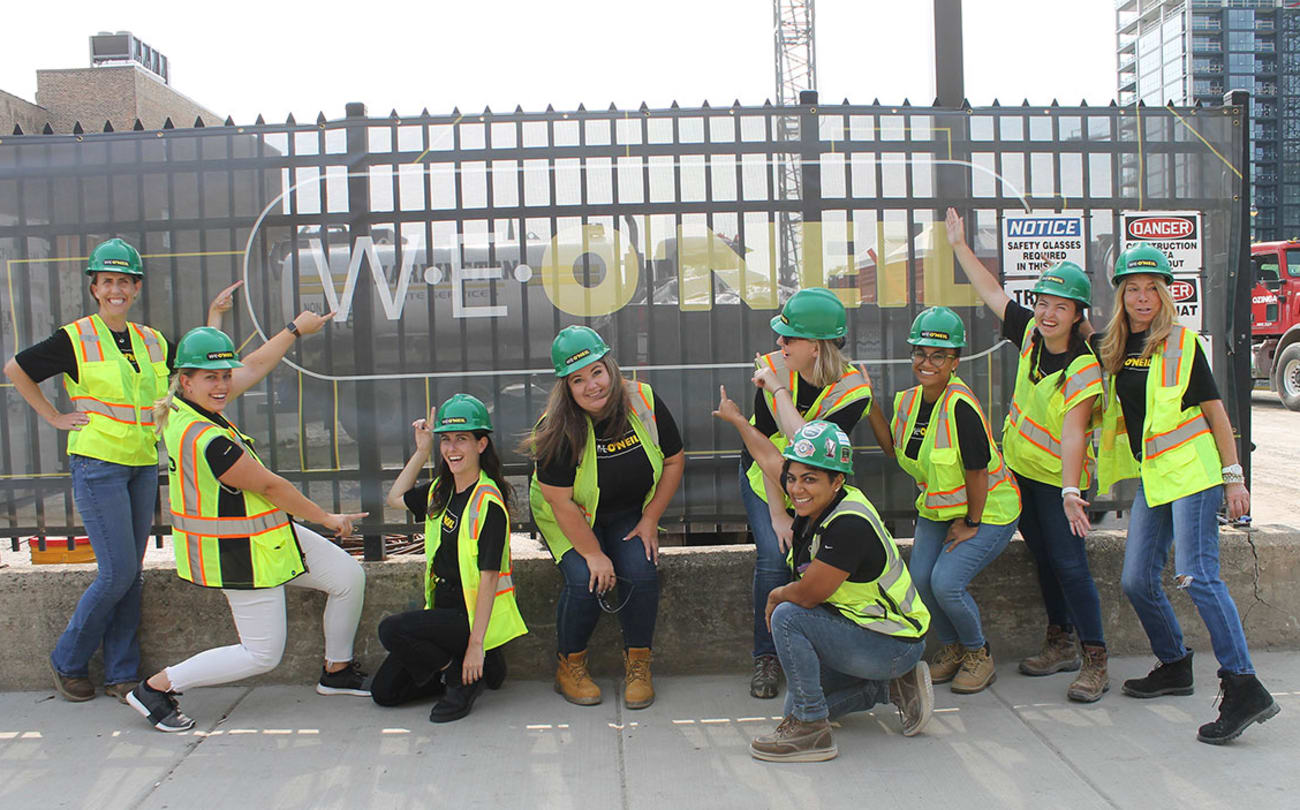 Group of W.E. O'Neil employees at a jobsite pointing to a company sign with many smiles.
