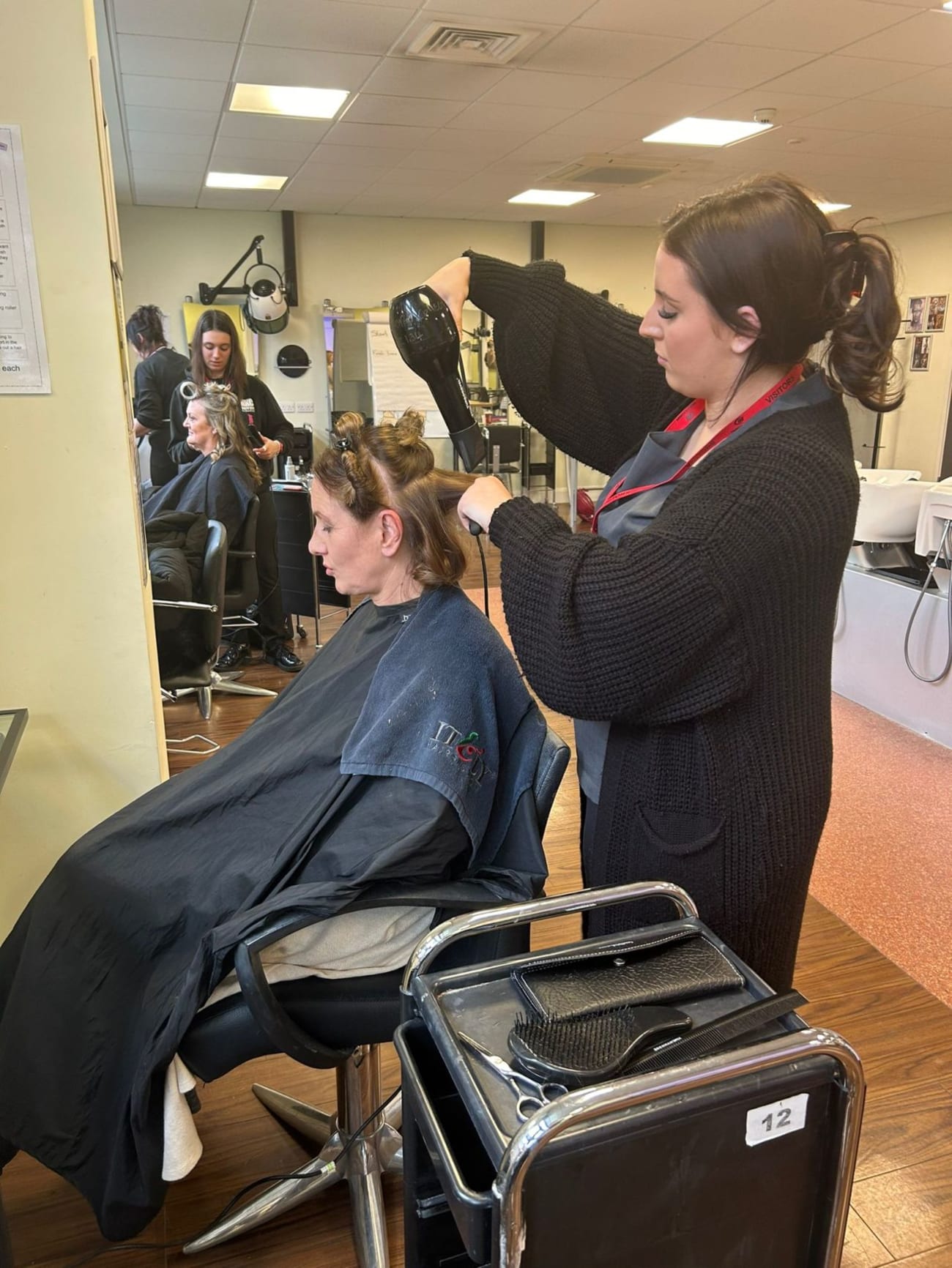 A Hairdressing student using a hairdryer to style a model's hair.