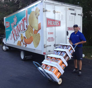 Route Sales employee standing next to a truck with a hand cart full of Herr’s product