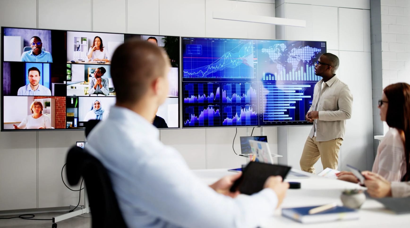 Three people in a room looking at two screens on a wall