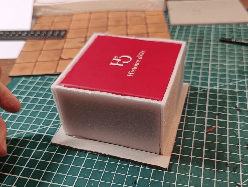Box mounted on cardboard base with foam slices around perimeter
