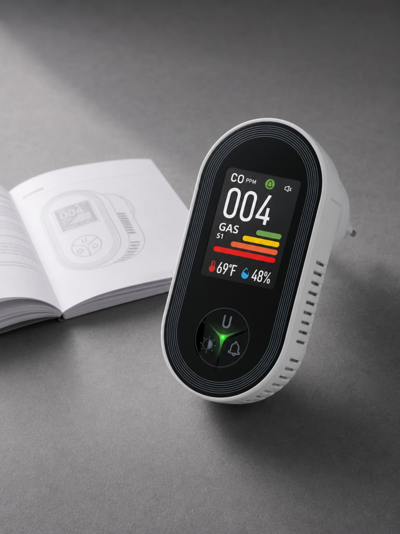 VIGILOX 4-in-1 plug-in CO and combustible gas monitor with color IPS display, alongside the included user manual, on a matte slate-grey surface — premium product packshot.
