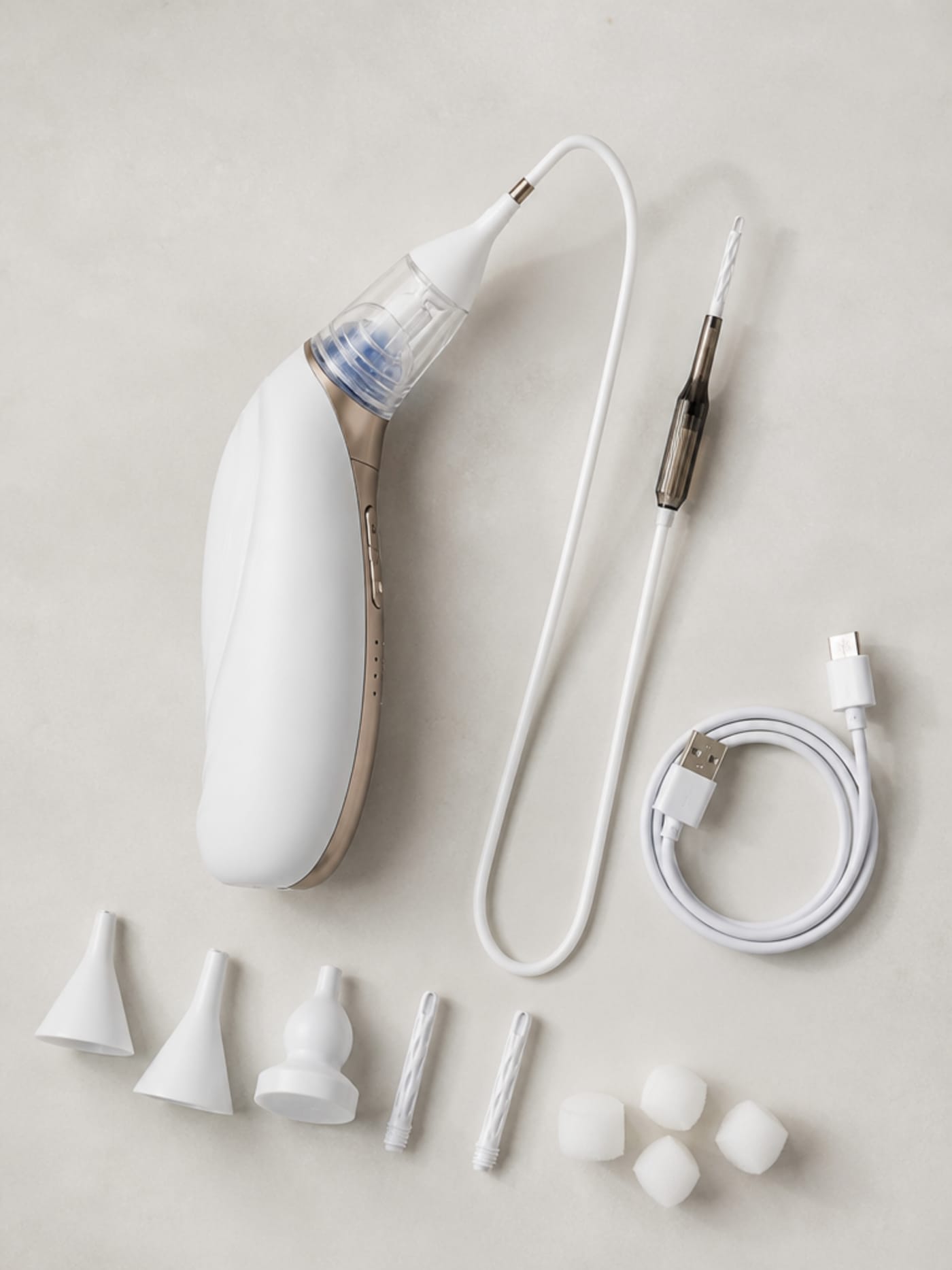 Vacurio device flat-lay packshot with silicone tip set fanned out and charging cable coiled neatly on a clean surface