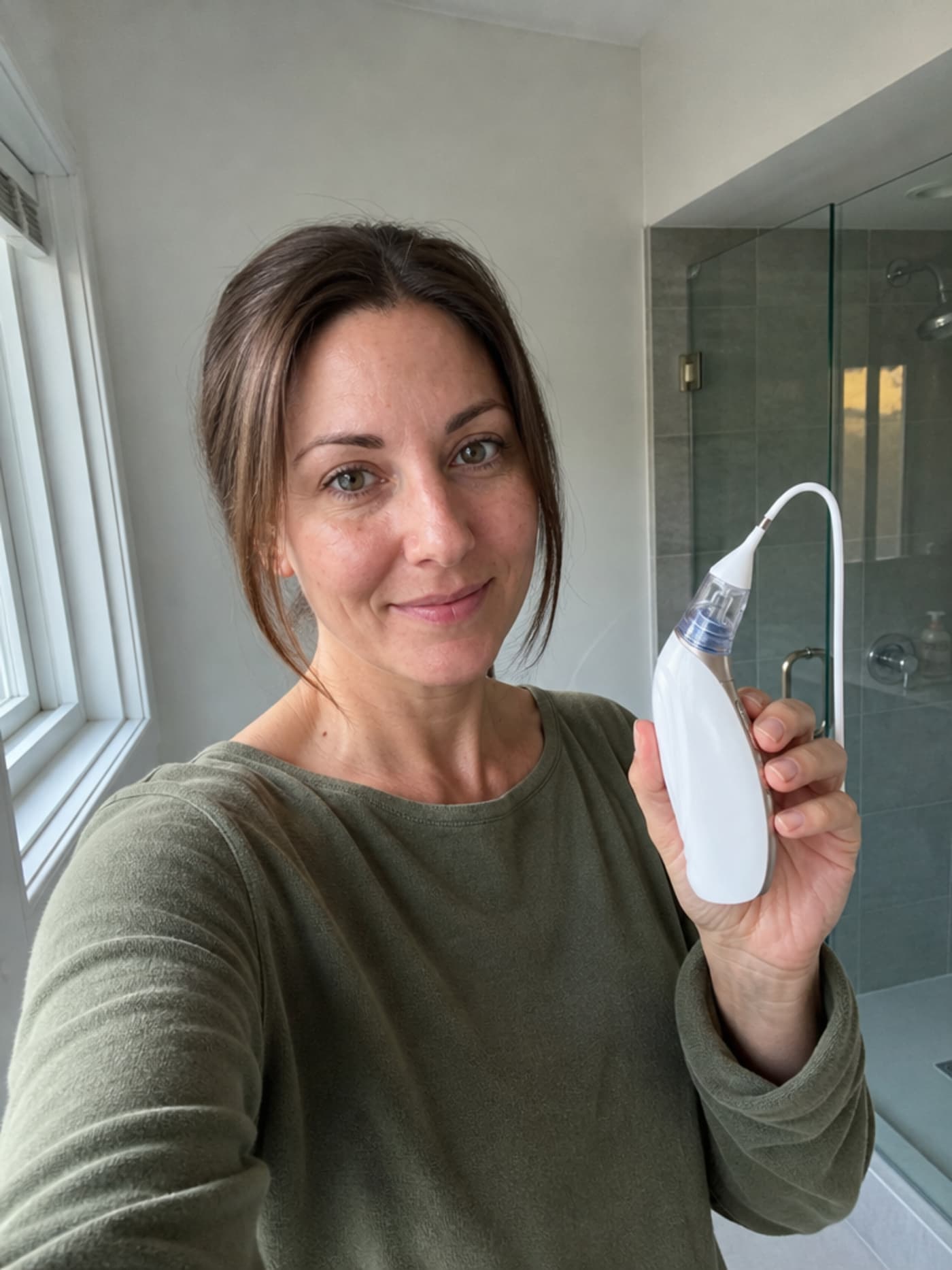 Woman in her mid-forties, olive-green top, selfie holding Vacurio device in home bathroom