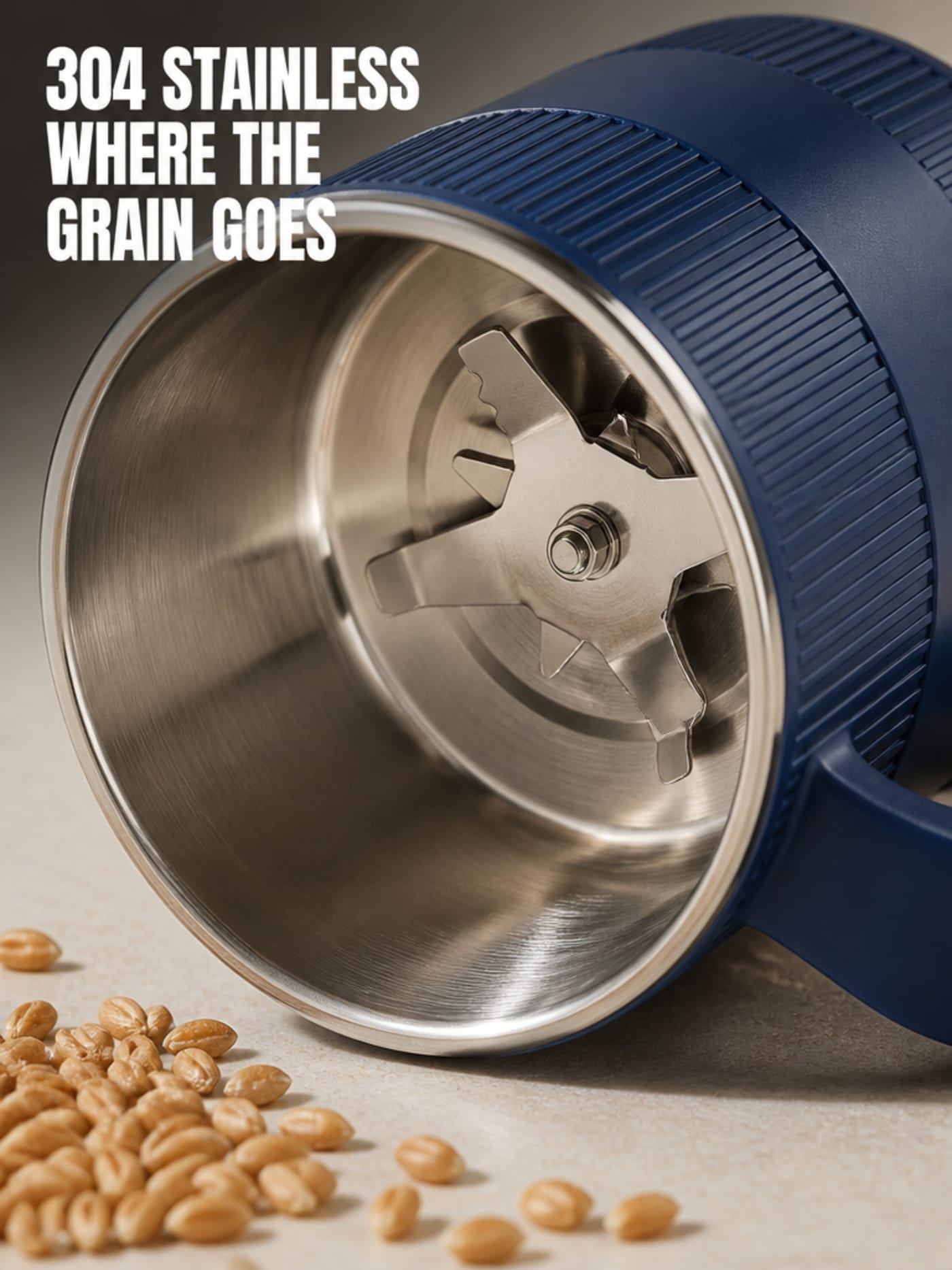 Macro close-up of the Grainbloom's 304 stainless steel grinding chamber surface with scattered whole wheat berries in the foreground