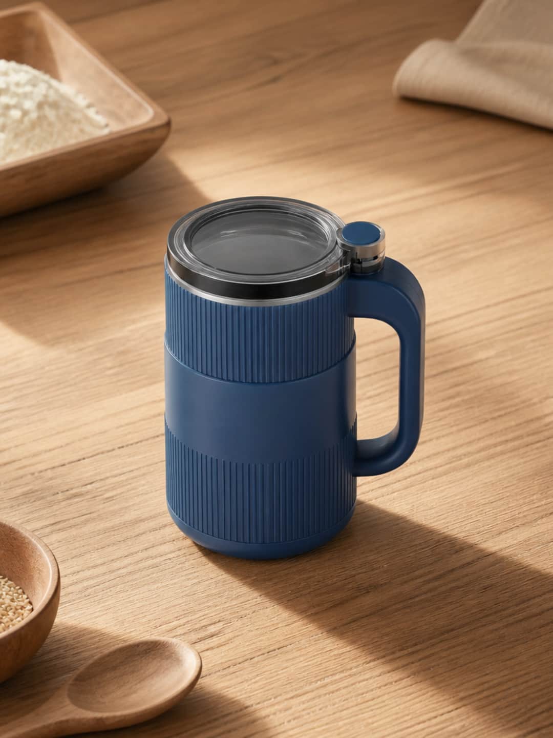 Grainbloom grain mill and Fresh-Milled Baking Guide on a warm wood kitchen counter, with whole wheat berries scattered at the base of the mill — the complete bundle as it arrives.