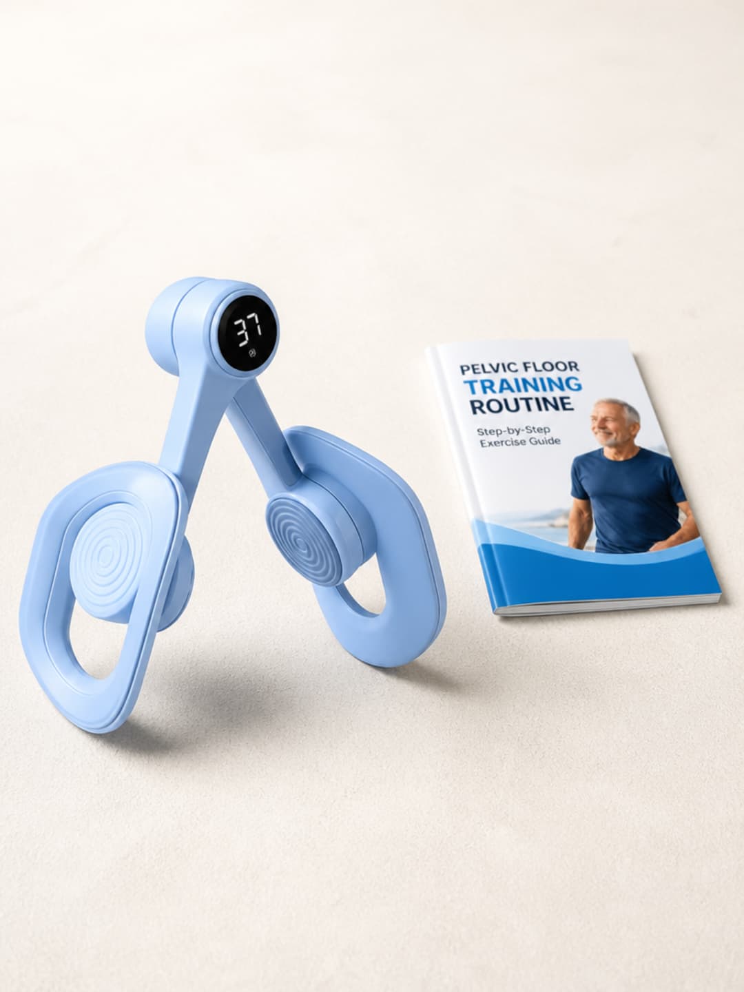 Pelvexia trainer and printed pelvic floor training guide on a warm off-white surface — light-blue matte body, soft TPE pads, digital counter visible