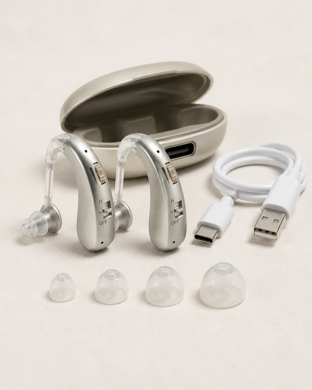 Two cream-colored Audexa behind-the-ear hearing devices as a matched pair, with travel case, four silicone ear-tip sizes, and USB charging cable arranged on a clean surface.