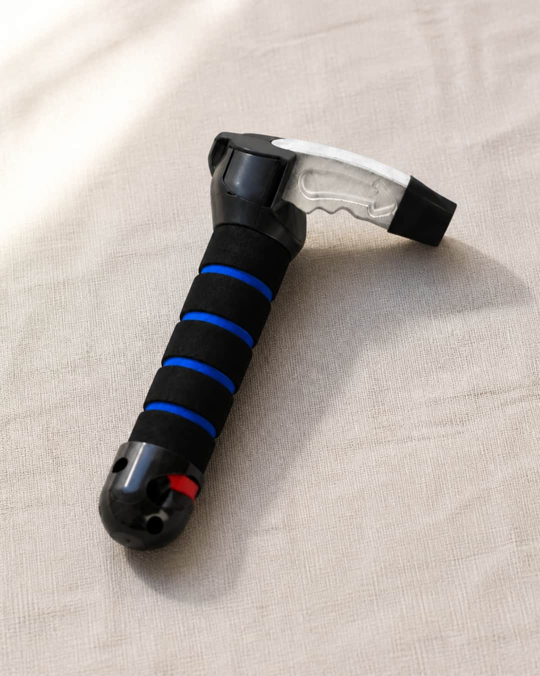 Car Aid Exit handle unit resting on a warm grey linen surface — padded non-slip grip and metal latch tip visible in a clean three-quarter product view