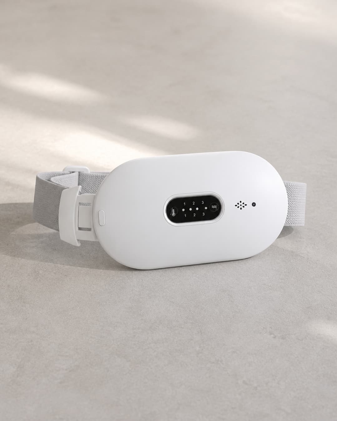 DayDefender wearable menstrual comfort belt laid flat on a pale stone surface — the single unit shown centered as a premium product packshot
