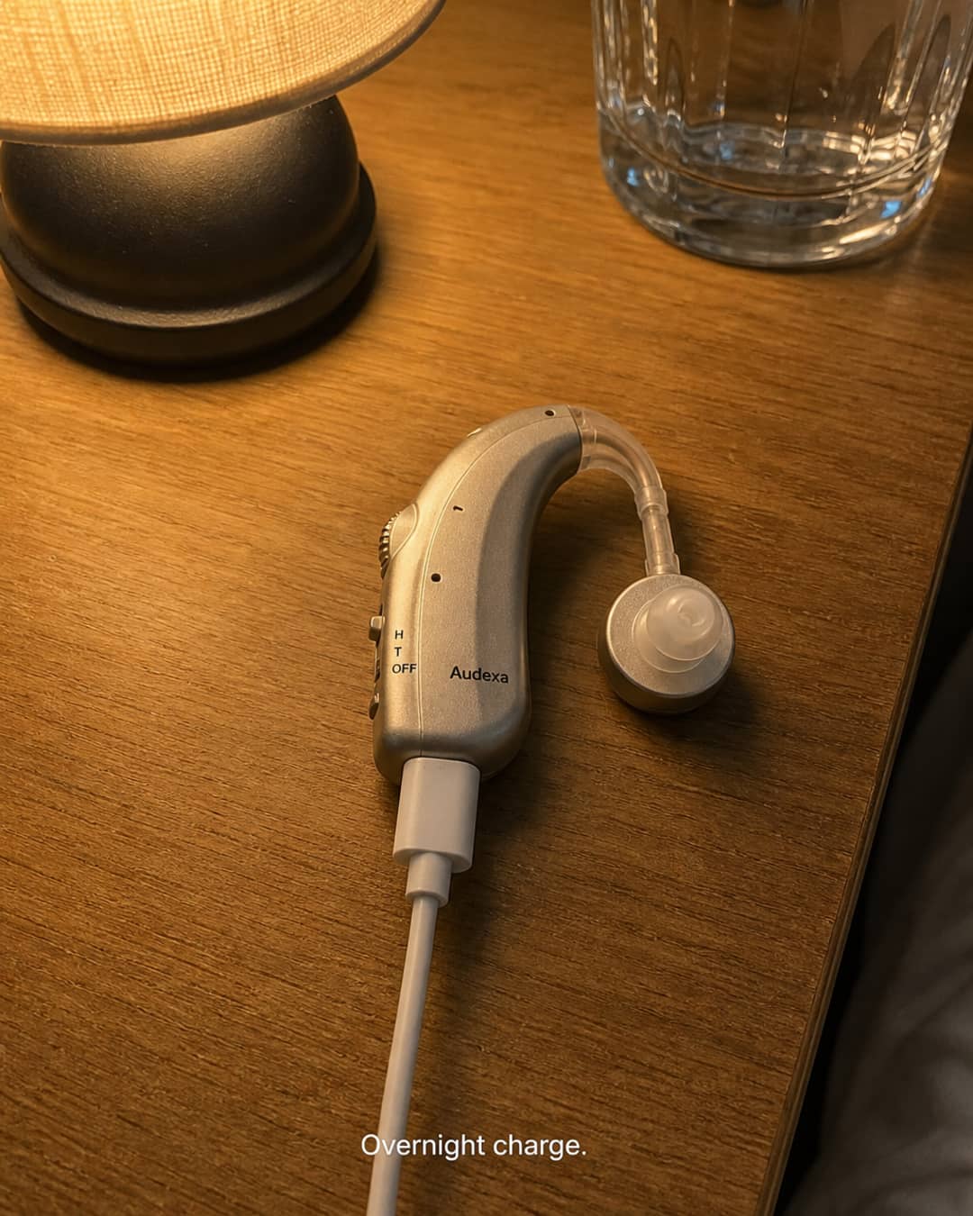 Illustrative tabletop photo of an Audexa device connected to a charging cable