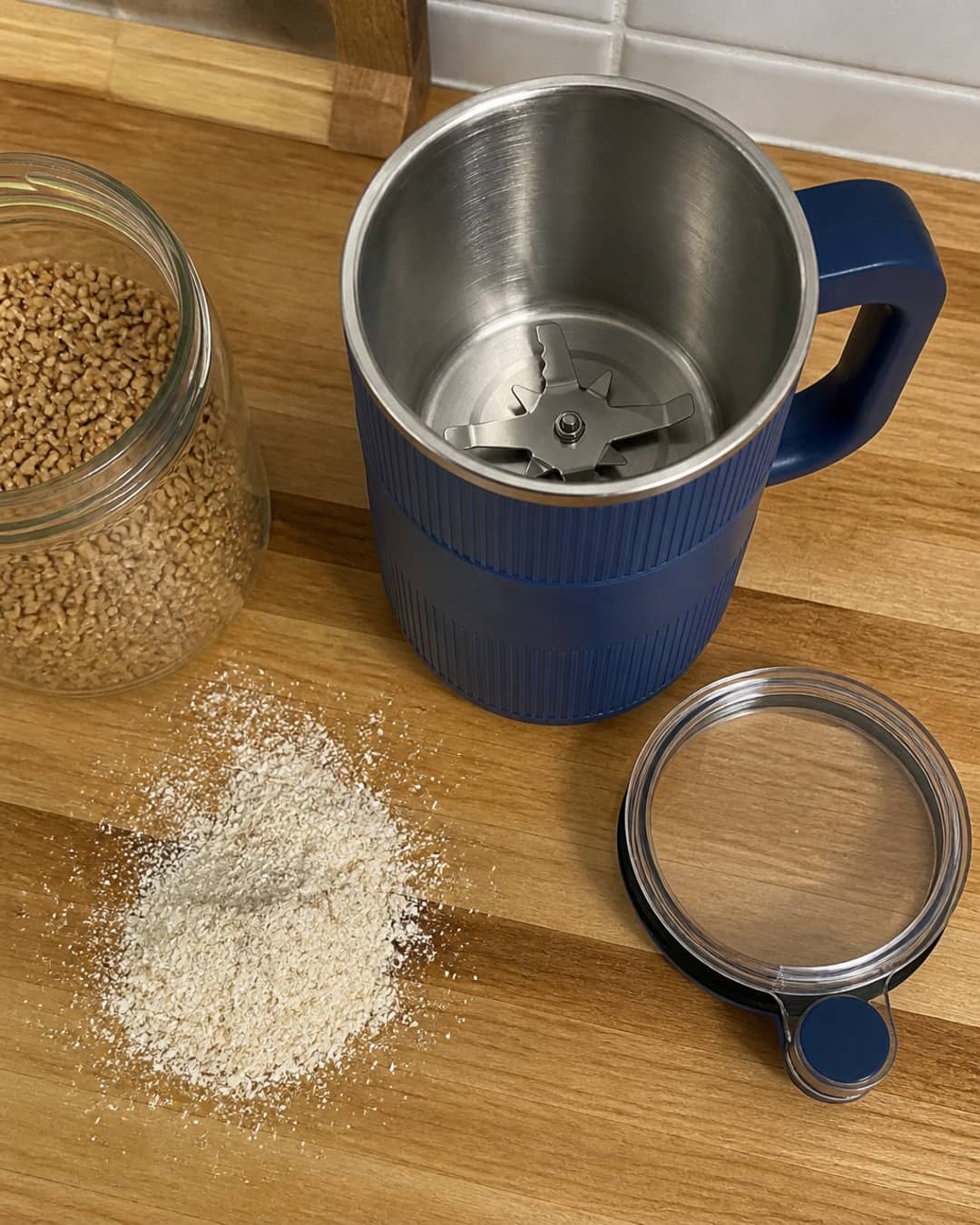 GRAIN BLOOM mill with lid off on a butcher-block counter beside grain berries and milled flour