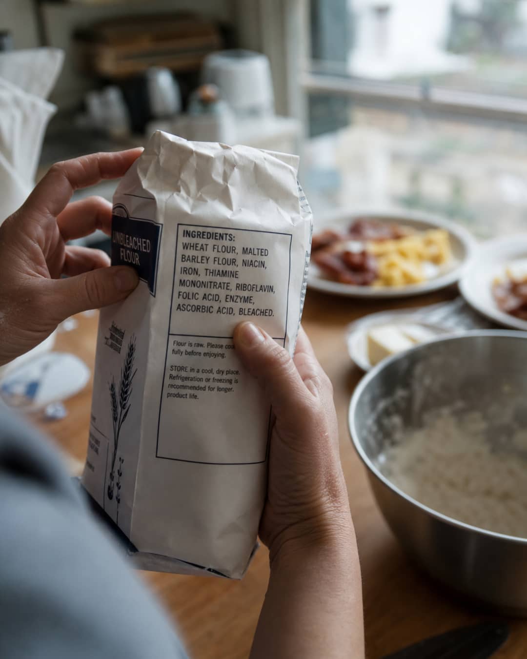 Hands holding a supermarket flour bag close to the ingredient panel that lists bleached flour