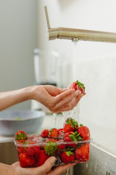 Person rinsing container of strawberries at sink