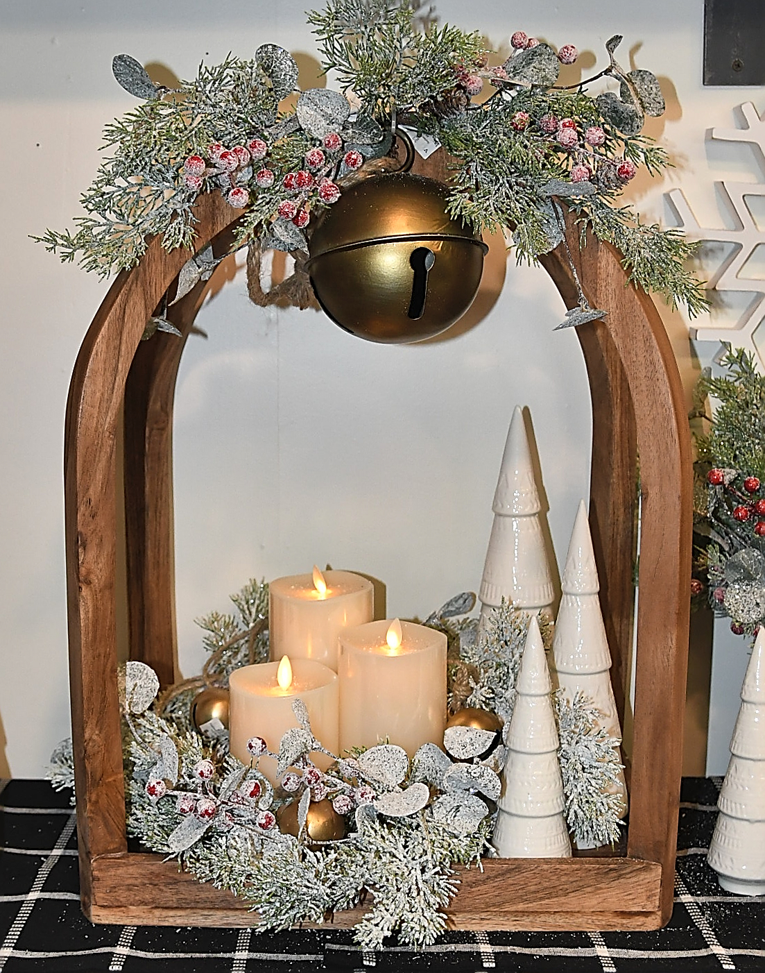 Handcrafted Christmas decoration with a wooden lantern holding candles, greenery, Christmas tree decor, and a large bell.