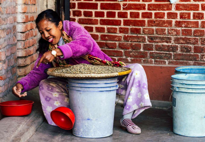 A woman laughs beside drying trays of coffee