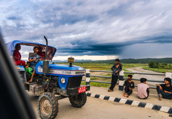 A tractor on a valley road under a monsoon sky
