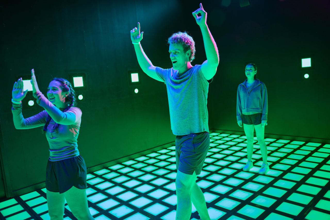 Players raise their arms in celebration on the illuminated floor grid.