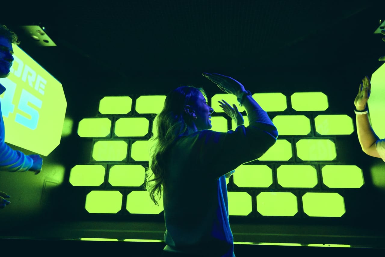 A player takes aim at a wall of glowing green bricks in the Strike room.