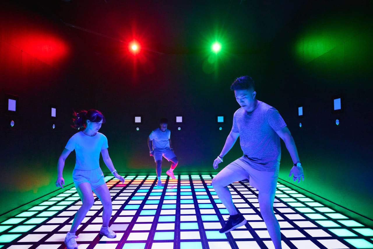 Players move across the illuminated floor grid beneath red and green lights.