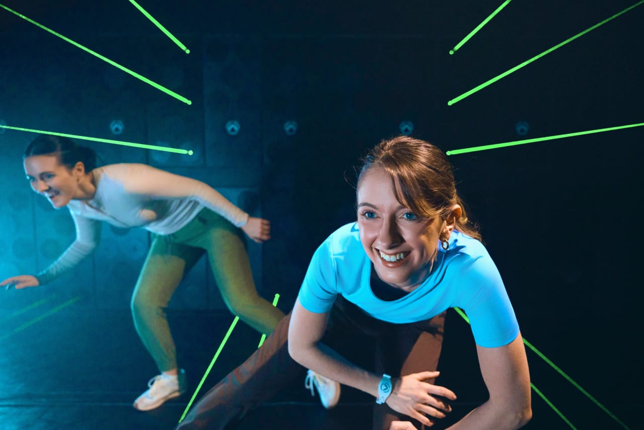 Two players smile as they navigate through green laser beams.