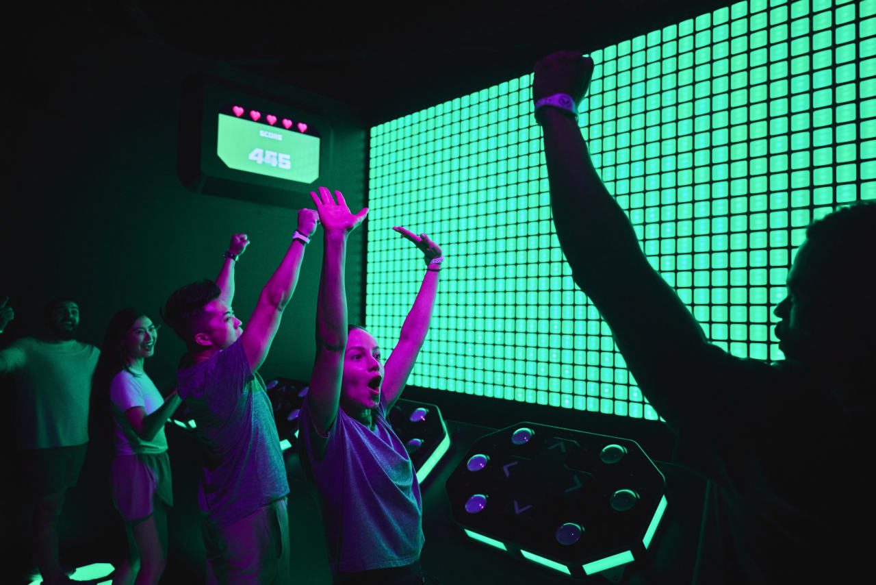 Players cheer with arms raised in front of the Control room's glowing green screen.