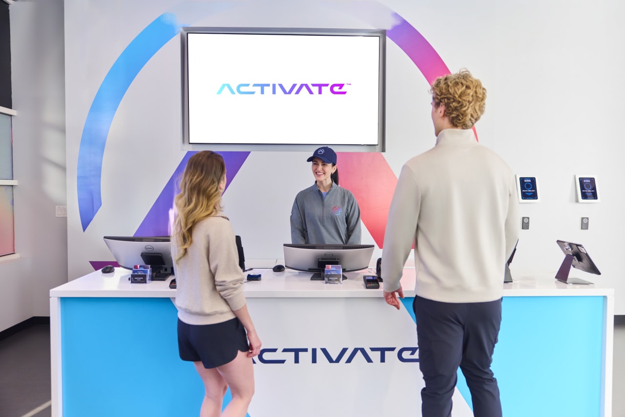 Guests at the Activate front desk beneath the lobby's branded screen.