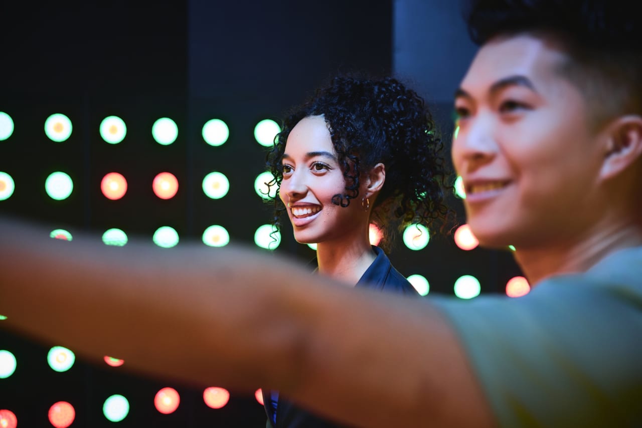 Two players smile as they reach for lights on the Press wall.