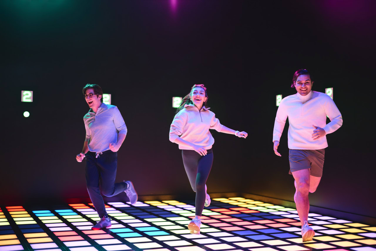 Three players race across a rainbow-lit floor grid.