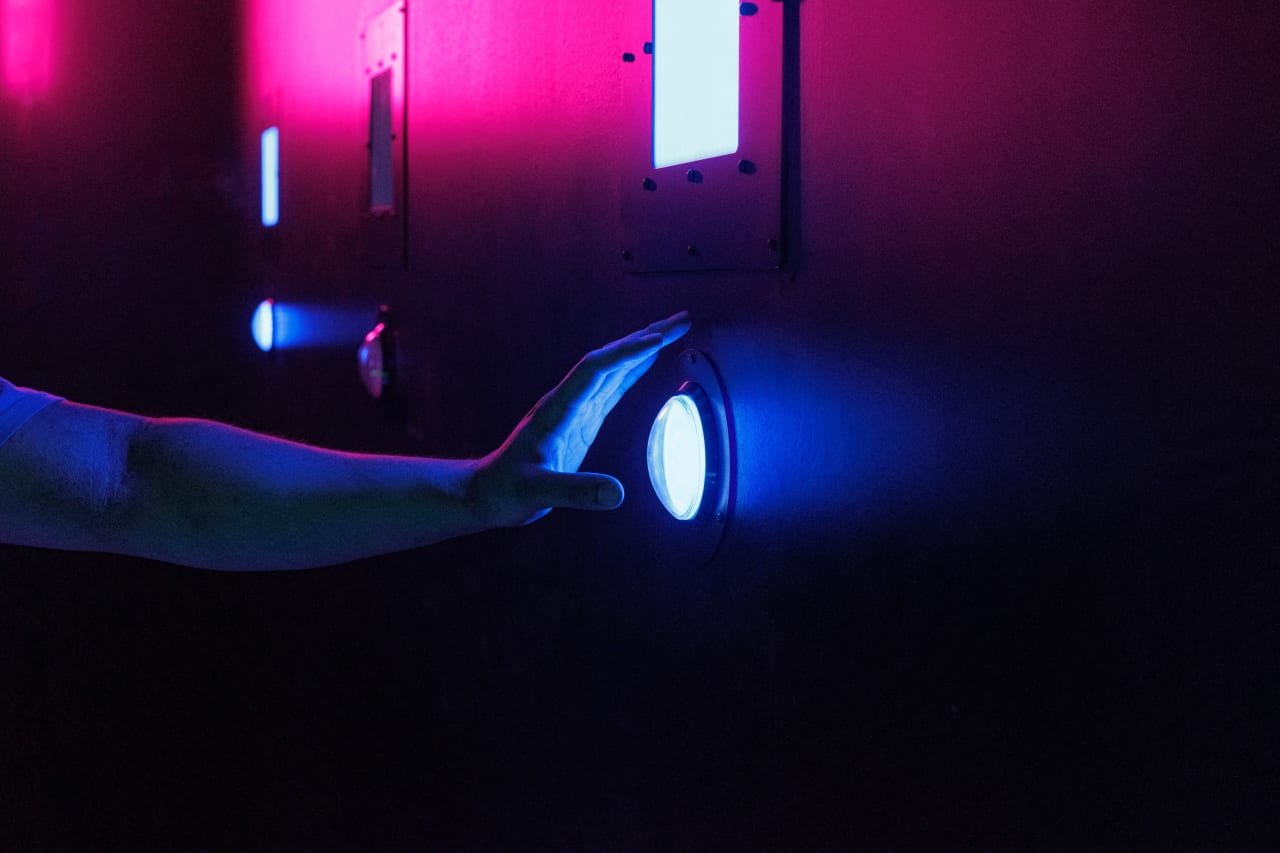 A hand reaches toward a glowing button in a darkened room.