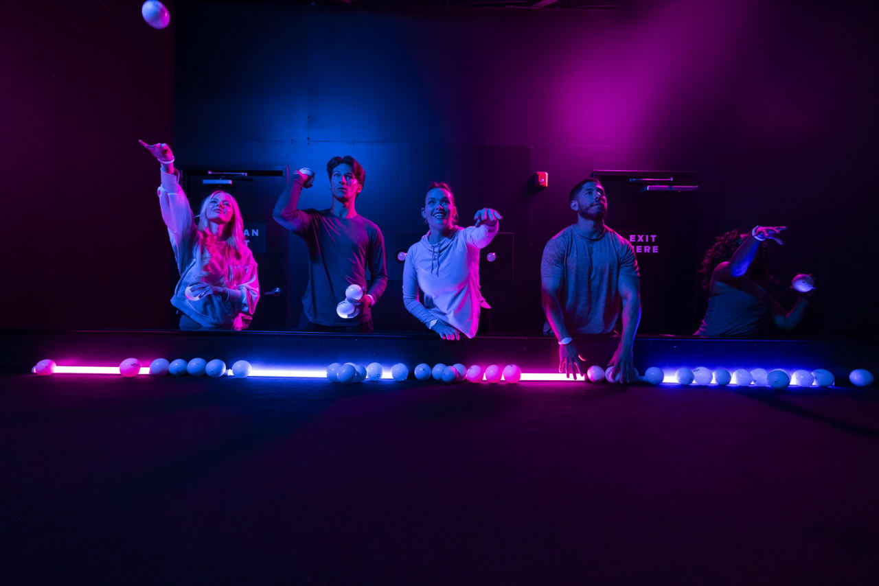 Four players line up behind a rail of glowing balls in a darkened room.
