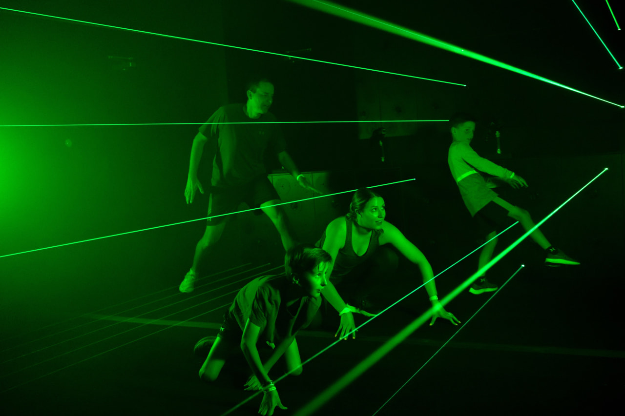 A family moves through a room criss-crossed with green laser beams.