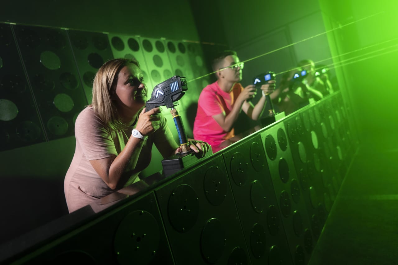 Two players aim light blasters at a green-lit target wall.